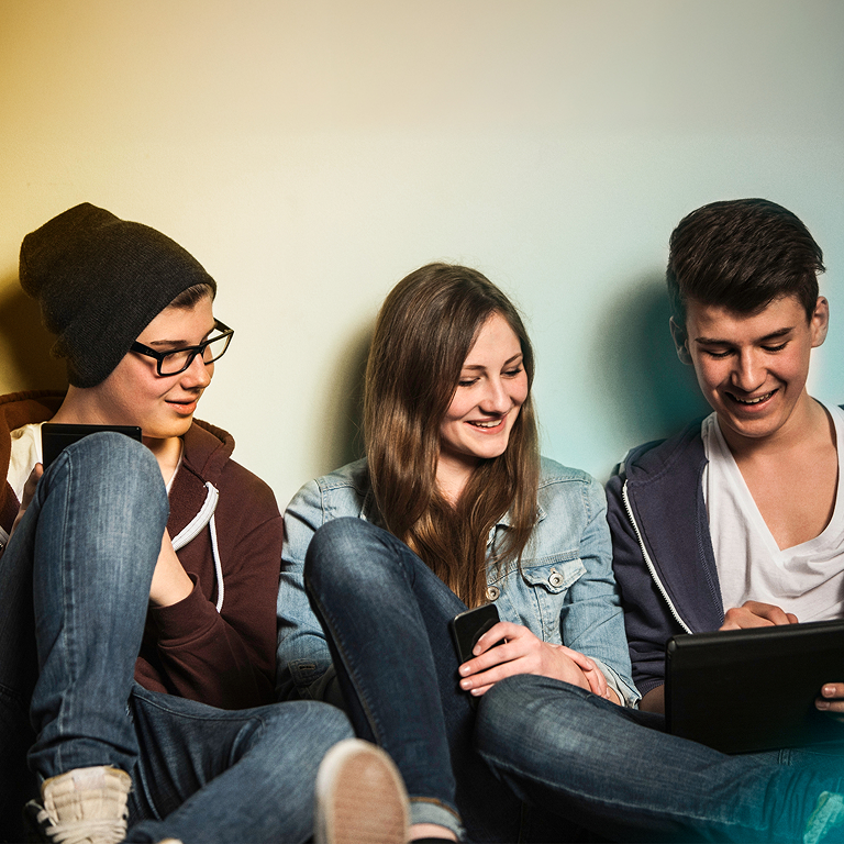 Skupina mladých ľudí sediacich na zemi používa smartfón a tablet – vizuál projektu Digitálny štart pre partnerov.